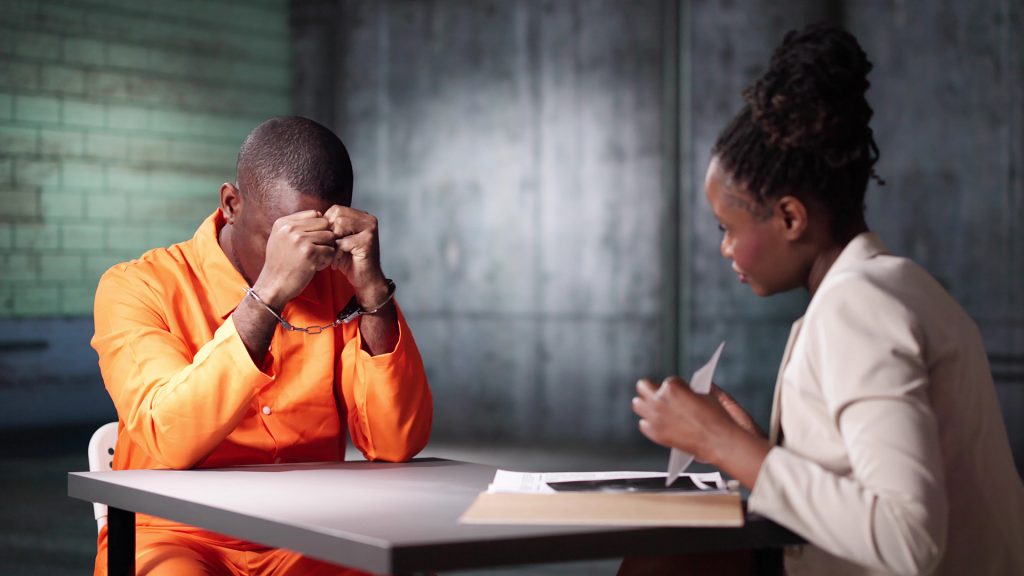 criminal-defense A lawyer in a suit speaking with a person behind jail bars, symbolizing legal representation for individuals in custody or facing criminal charges.