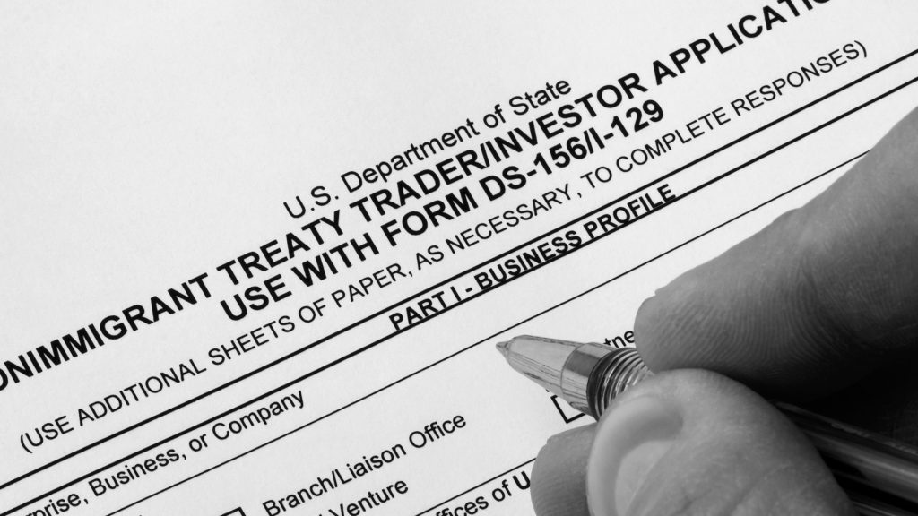 investor-visa-lawyer Image of a professional investor shaking hands with an attorney over legal documents, with an American flag and business charts in the background—symbolizing investor visas and U.S. immigration through investment.