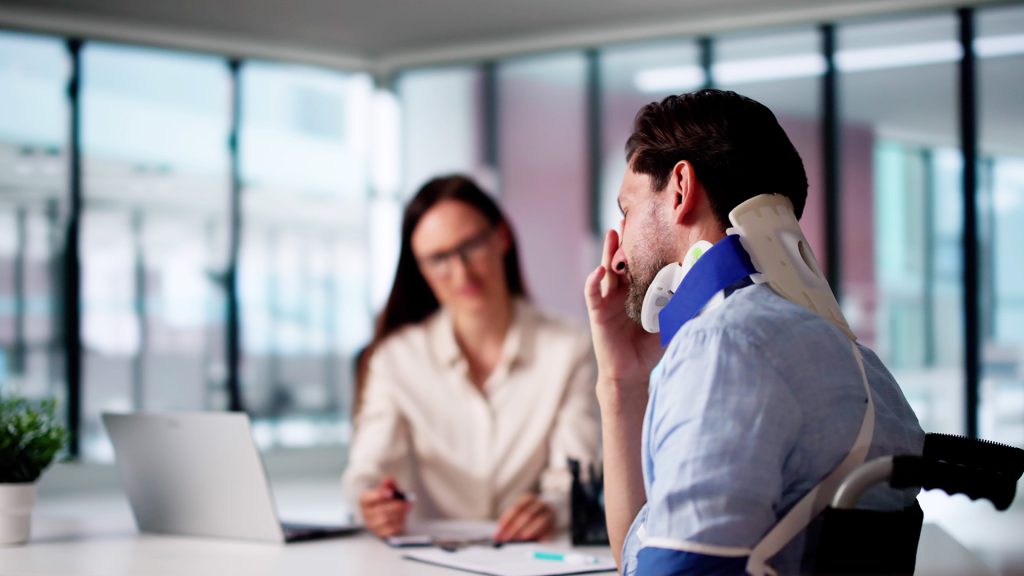 Injured person wearing a sling sitting at a desk with a lawyer in a suit, reviewing documents together in a professional office setting.